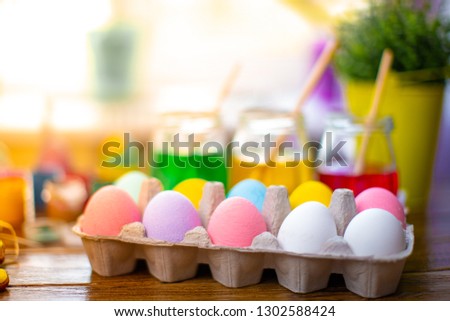 Background with colorful eggs in basket, paints, brushes. Wooden table decorating for holiday.