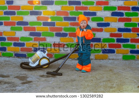 Happy boy in bright suit with a vacuum cleaner and candy against background of multi-colored brick wall. Romantic lighting with reflection of sunlight. Effect of lens flares without post-production