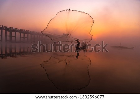 Silhouette Asian fisherman on wooden boat casting a net for freshwater fish at U Bein Bridge,Mandalay, Myanmar (Burma) in the early morning before sunrise 