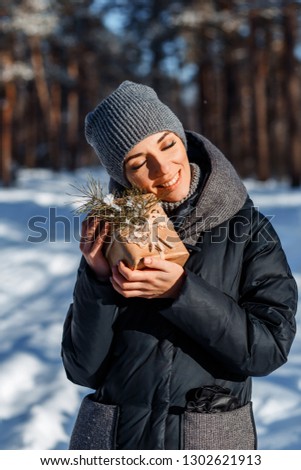 A vertical picture of a woman with a present in forest on a sunny winter day