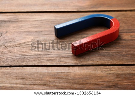 Red and blue horseshoe magnet on wooden background. Space for text