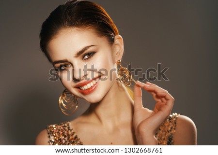 A cheerful glamorous woman wearing a gold dress is holding on to her earrings