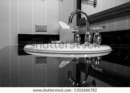 White sink with chrome taps for hot and cold water on black marble plate