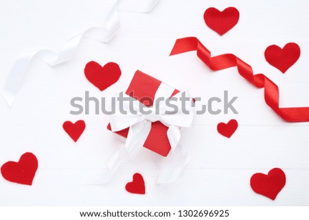 Gift box with ribbon bow and red hearts on white wooden table