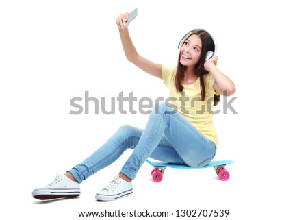 Young girl sitting on skateboard with headphones and making selfie