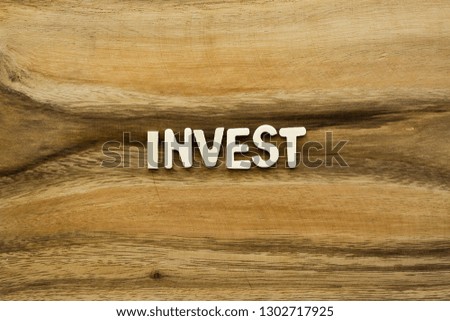 Plywood alphabets on acacia wooden texture background concept. The word "INVEST" on wood pattern backdrop.