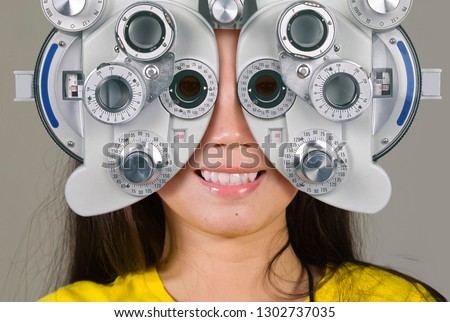 young woman smiling happy looking through optometric hospital device and checking eyes having sight exam in ophthalmology health care isolated on grey background Royalty-Free Stock Photo #1302737035
