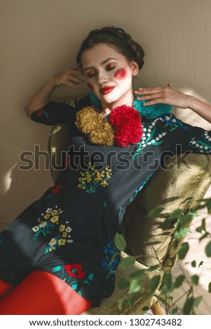 Fashionable beautiful brunette happy girl in a jumpsuit with floral embroidery with color makeup: red cheeks and lips. Granny chic style. Retouched portrait.Conceptual photo