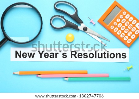 New year resolutions on sheet of paper with pencils, scissors, calculator and magnifying glass