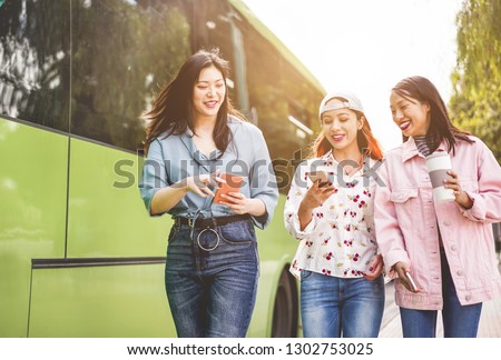 Happy asian friends using smartphones at bus station - Young students people having fun with technology trends after school outdoor - Friendship, university and trasports app concept - Focus on faces Royalty-Free Stock Photo #1302753025