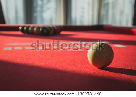 Billiards pool game on red table. Close up on a white ball with racked up triangle of billiard balls background