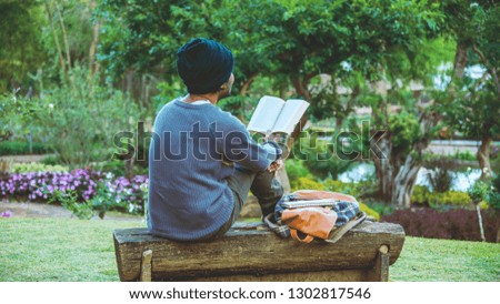 The young man was reading a book at the park. Among the natural trees and beautiful flower garden