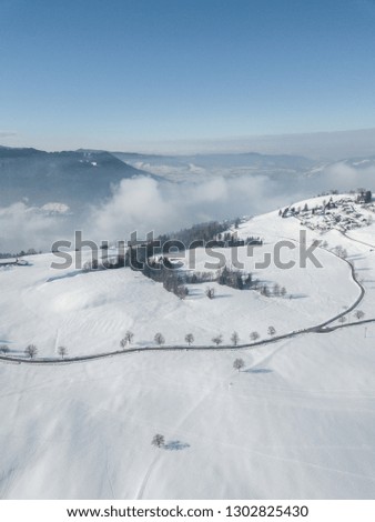 Aerial view of snow covered landscape in Switzerland, Europe. Tranquil scene with white terrain and forest covered mountains and fog in the background.