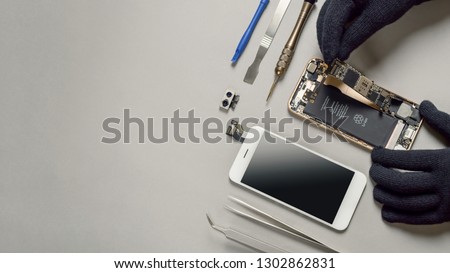 Technician or engineer disassembling components broken smartphone and take off logic board for repair or replace new smartphone logic board on desk  Royalty-Free Stock Photo #1302862831