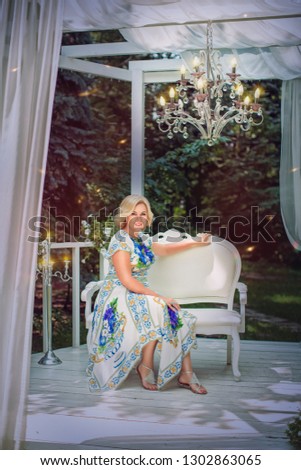 Happy woman blonde in colorful dress resting on sofa in gazebo in park