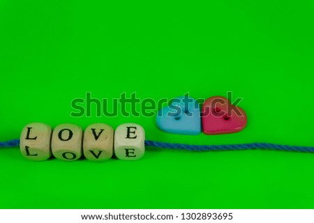 Red and blue heart shaped buttons and word Love on blocks threaded on strings over a colorful green background for romantic or Valentines concepts with free copy space for text