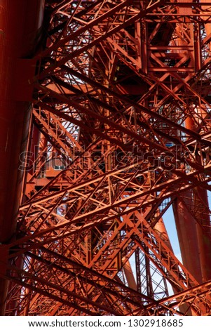 Photograph looking up into the beams and girders of the iconic Forth Rail Bridge, Edinburgh, Scotland.  One area of stability amongst the apparent chaos is a cabin camouflaged by the same red colour.