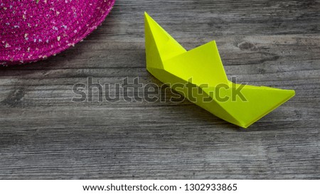 Origami, yellow ship of paper and pink hat on wooden table