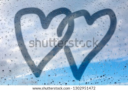 Picture of two hearts on a misted glass. Glass window with raindrops against the blue sky. Concept of love and friendship. Valentines day card concept. Heart for Valentines Day Background.