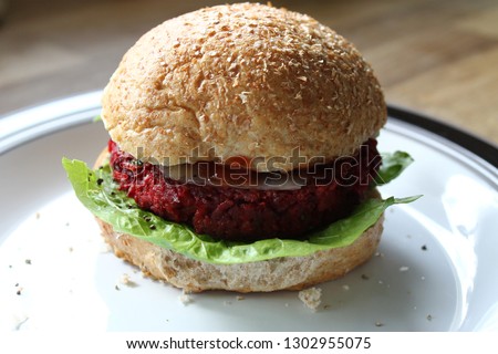 Veggie, vegetarian, dietary fiber-rich beetroot and chickpea burger served horizontally on a white plate. Closeup with rustic wooden background