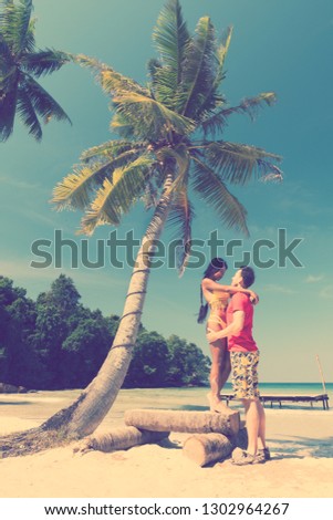 A loving couple enjoying the breathtaking views of the tropical sandy beach with green coconut palm trees and beautiful clean sea ocean on a background of blue sky