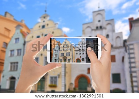 A man is making a photo of building complex of old buildings - The Three Brothers - Riga, Latvia on a mobile phone