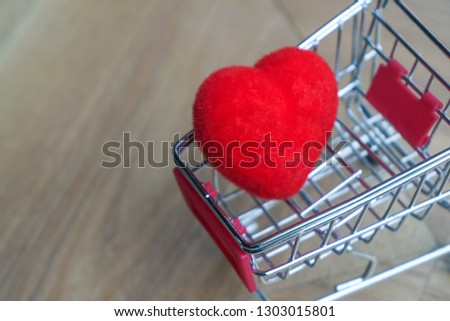 A red heart in mini shopping cart on wooden table                              