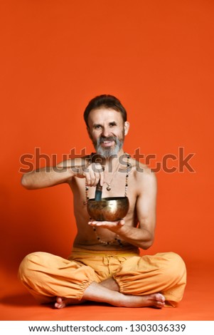 elderly man with a gray beard yogi in good physical shape holding singing bowl Tibetan musical instrument . Man plays Nepalese Himalayan instrument souvenir for meditation. Sound therapy melody yoga