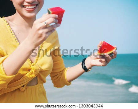 Attractive Young Asian woman standing by the sea,she holding fresh watermelon,tropical summer concept.