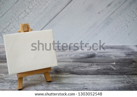 Small easel with a blank canvas over white. Old wooden background and big copy space for your sign and text