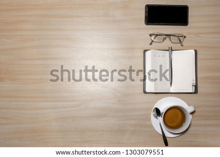 Desk with eyeglasses, notepad, smartphone, pen and a cup of tea on a wooden table. Top view with copy space. Flat lay - image