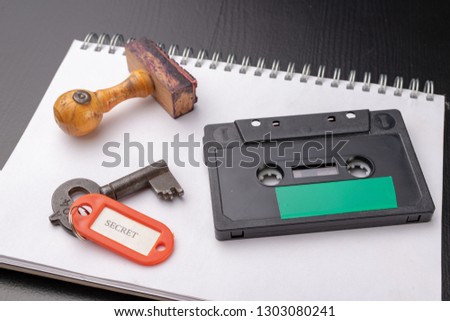 Old wooden stamp and a cassette tape on a white piece of notebook. A key to secret recordings of political talks. Dark background.
