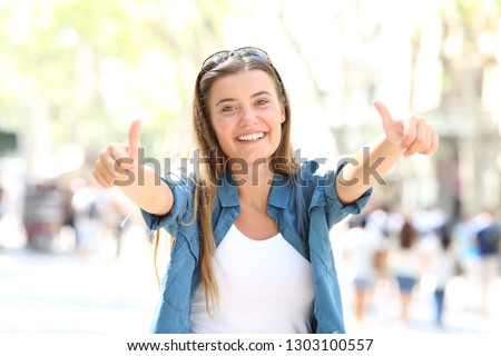 Front view portrait of a happy girl gesturing both thumbs up in the street