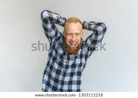 Red hair mature man standing isolated on grey wall hands behind head looking camera laughing playful