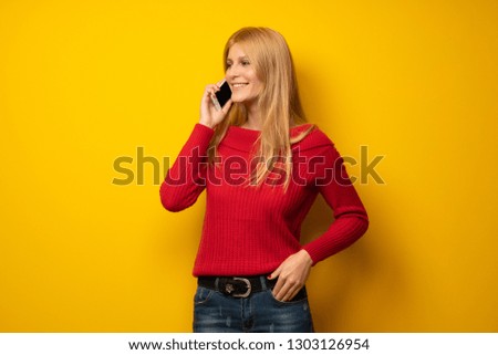 Blonde woman over yellow wall making a selfie