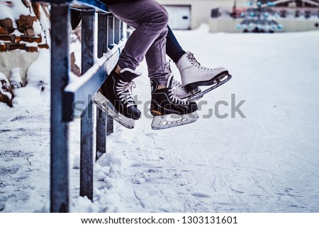Couple wearing ice skates sitting on a guardrail. Dating in an ice rink.
