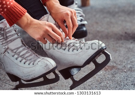 Young couple preparing to a skating. Close-up photo of their hands tying shoelaces of ice hockey skates in a locker room
