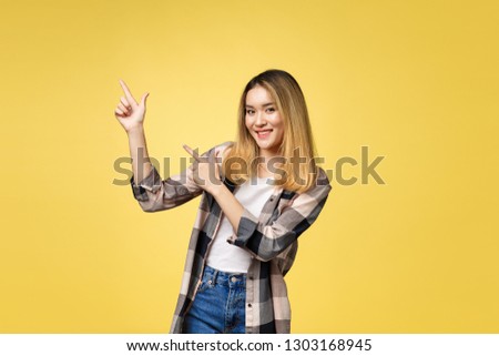Smiling woman pointing finger side. Isolated portrait on yellow.