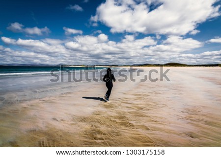 A young woman with curly hair running on Ardara Beach, County Donegal, Ireland