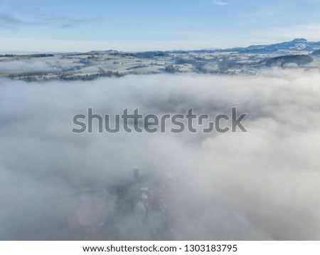 Above the clouds. Aerial view of of clouds and fog over rural area in Switzerland. Beautiful sunlight on cold winter morning with misty conditions.