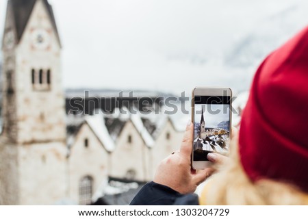 Woman in red hat taking picture of Hallstatt old Evangelische Pfarrkirche after snow storm, Austria.
