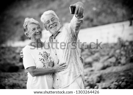 Black and white image retro concept filter - couple of happy smiling cheerful aged elderly people taking selfie picture with modern smart phone to share on internet social media accounts