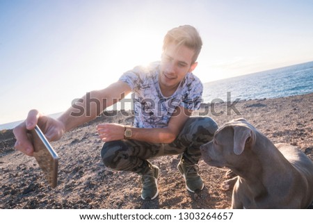 Best friends together young caucasian man and grey beautiful amstal dog taking selfie picture with smart phone outdoor with sunlight sunset in background - ocean and vacation concept