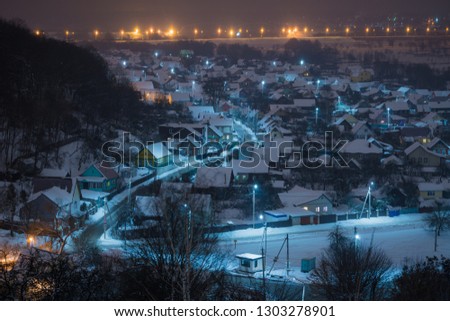 The road in the village in winter. Private sector on the outskirts of the city. View of the snowy town and the mountain with trees at night.