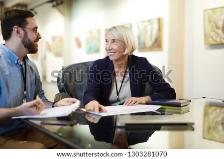 Portrait of two cheerful business people working at desk in modern gallery or museum, copy space Royalty-Free Stock Photo #1303281070