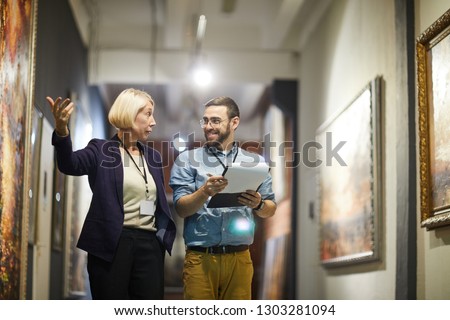 Portrait of two cheerful museum workers discussing paintings walking in art gallery, copy space Royalty-Free Stock Photo #1303281094