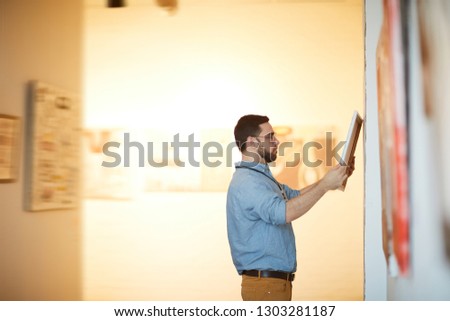 Side view portrait of bearded man holding picture in art gallery or museum, copy space Royalty-Free Stock Photo #1303281187