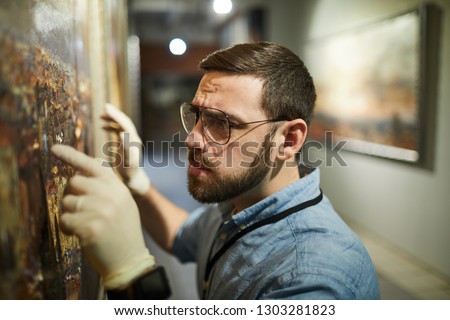 Close up  of bearded museum worker inspecting painting for restoration, copy space