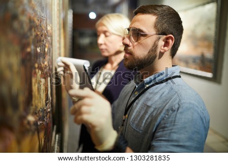 Waist up portrait of two museum workers inspecting painting for restoration, copy space