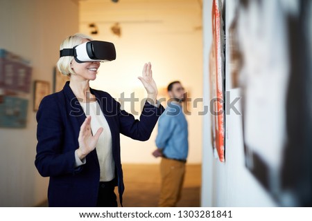 Waist up portrait of contemporary smiling woman wearing VR headset in art gallery, copy space Royalty-Free Stock Photo #1303281841